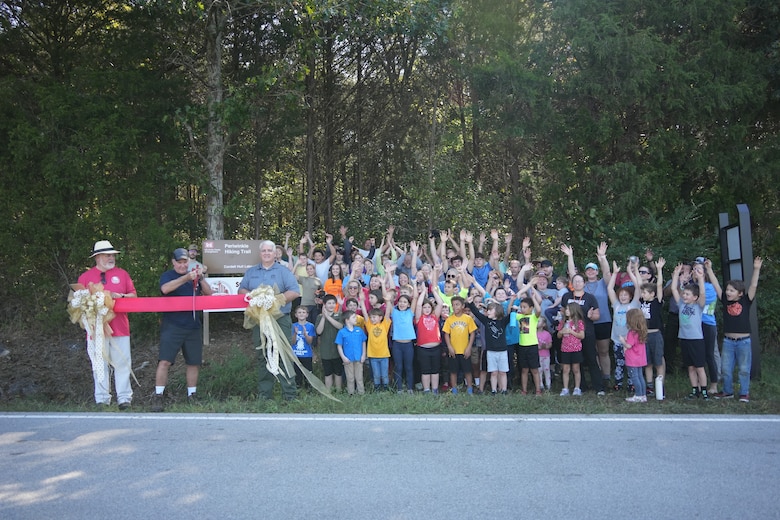Granville, Tenn. (Sept. 27, 2025) — John Deane (left), owner of Wildwood Resort & Marina, holds one end of the ribbon as Cordell Hull Lake volunteer Ted Tillman cuts it and Kenny Claywell holds the other end during the ribbon-cutting ceremony for the new Storybook Trail at Periwinkle Trail, with volunteers standing to their left. (USACE photo by Noe Gonzalez)
