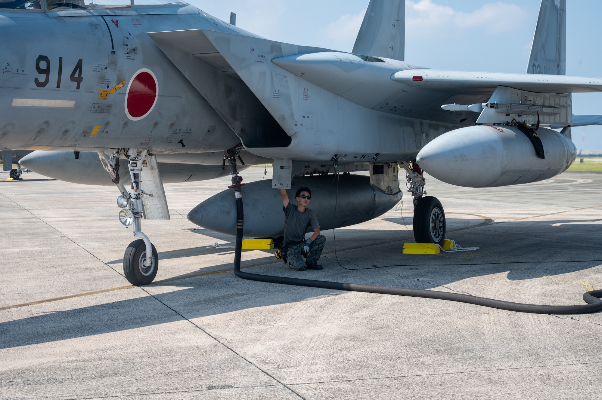 A service member sits under a jet, refueling it.