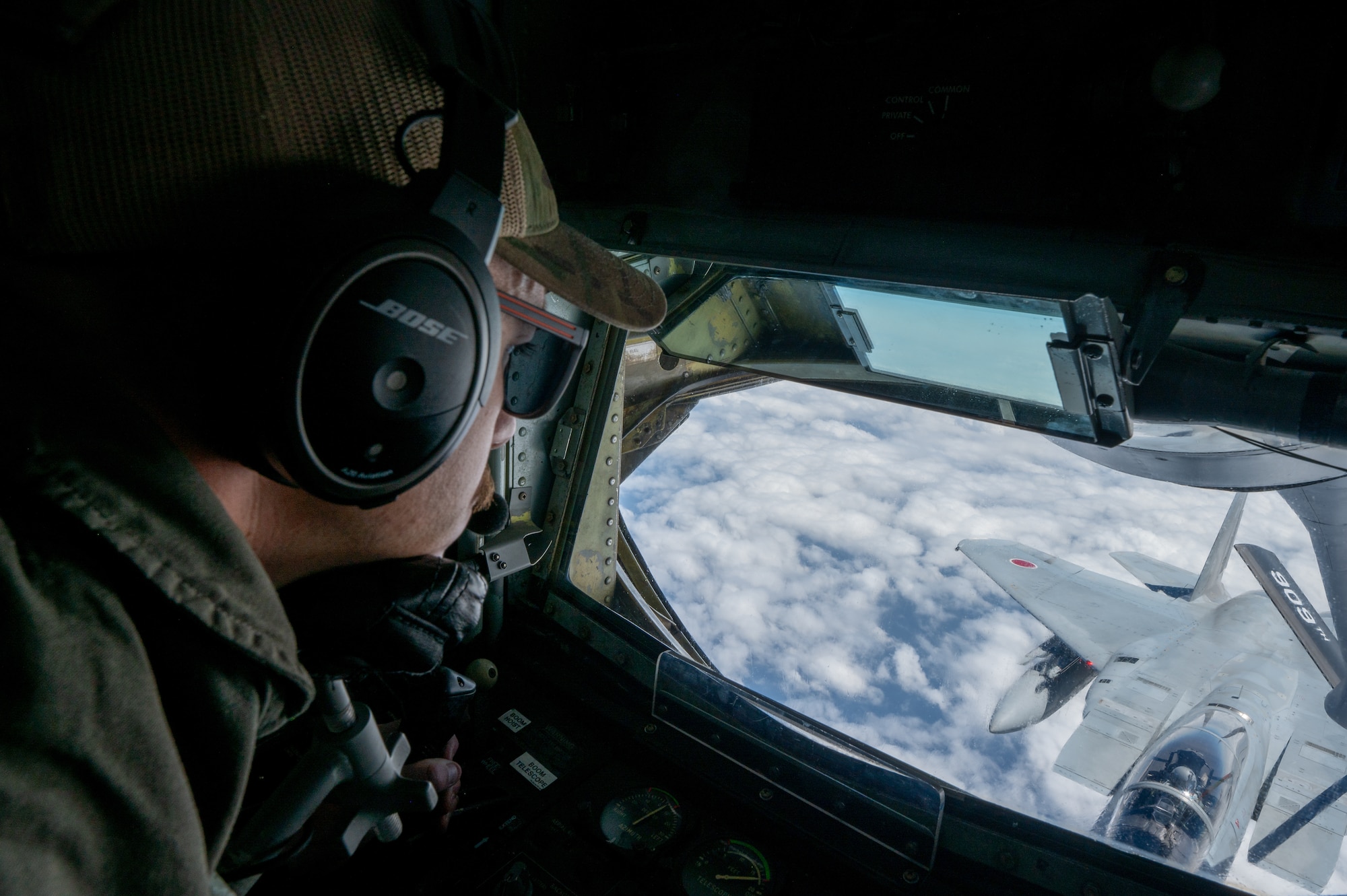 a military member looking out of a boom pod window looks at a fighter jet
