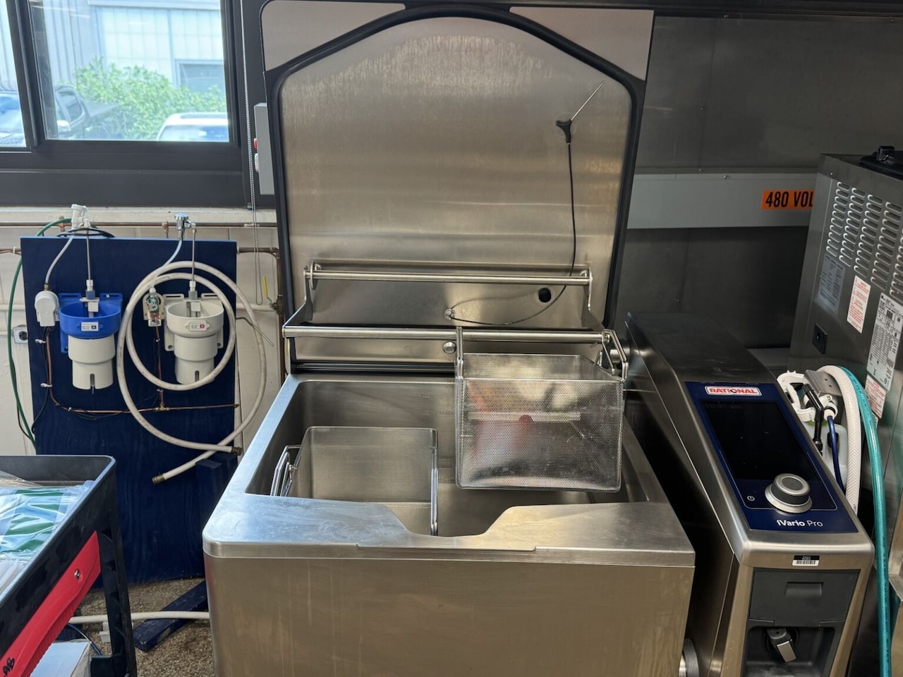 A large, stainless steel piece of equipment including two large drainage baskets is shown in a kitchen.