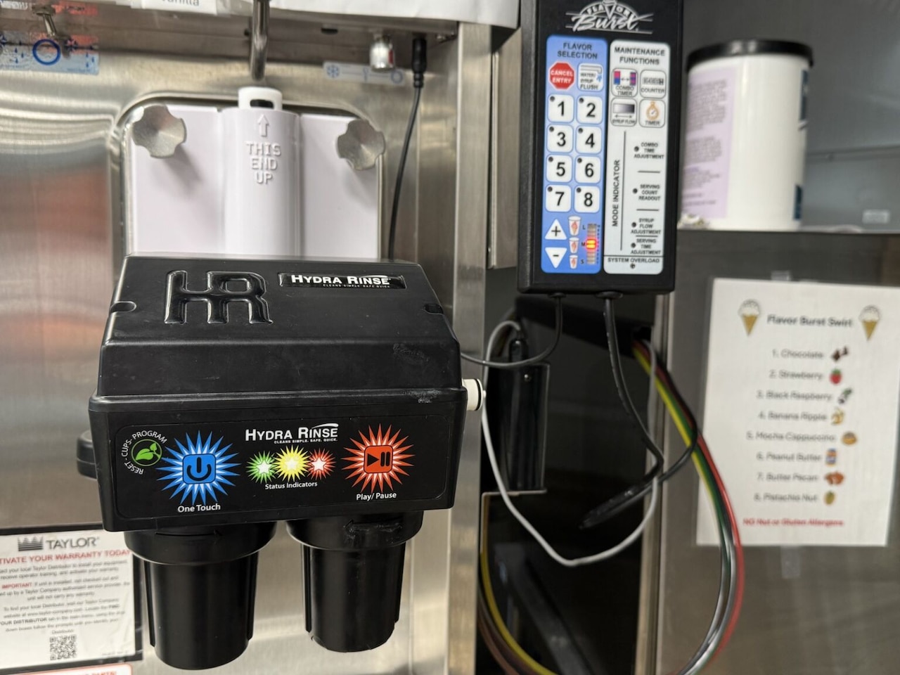 A piece of equipment and wires attach to a larger stainless steel piece of equipment that is used to clean an ice cream maker.