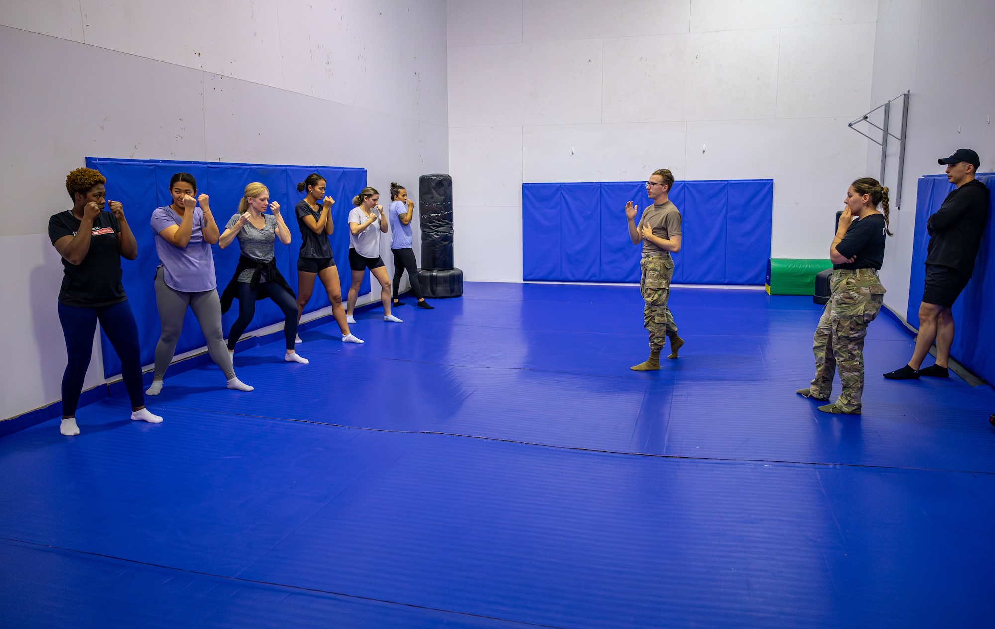 Airmen and participants practice self-defense basics in a room with blue mats.