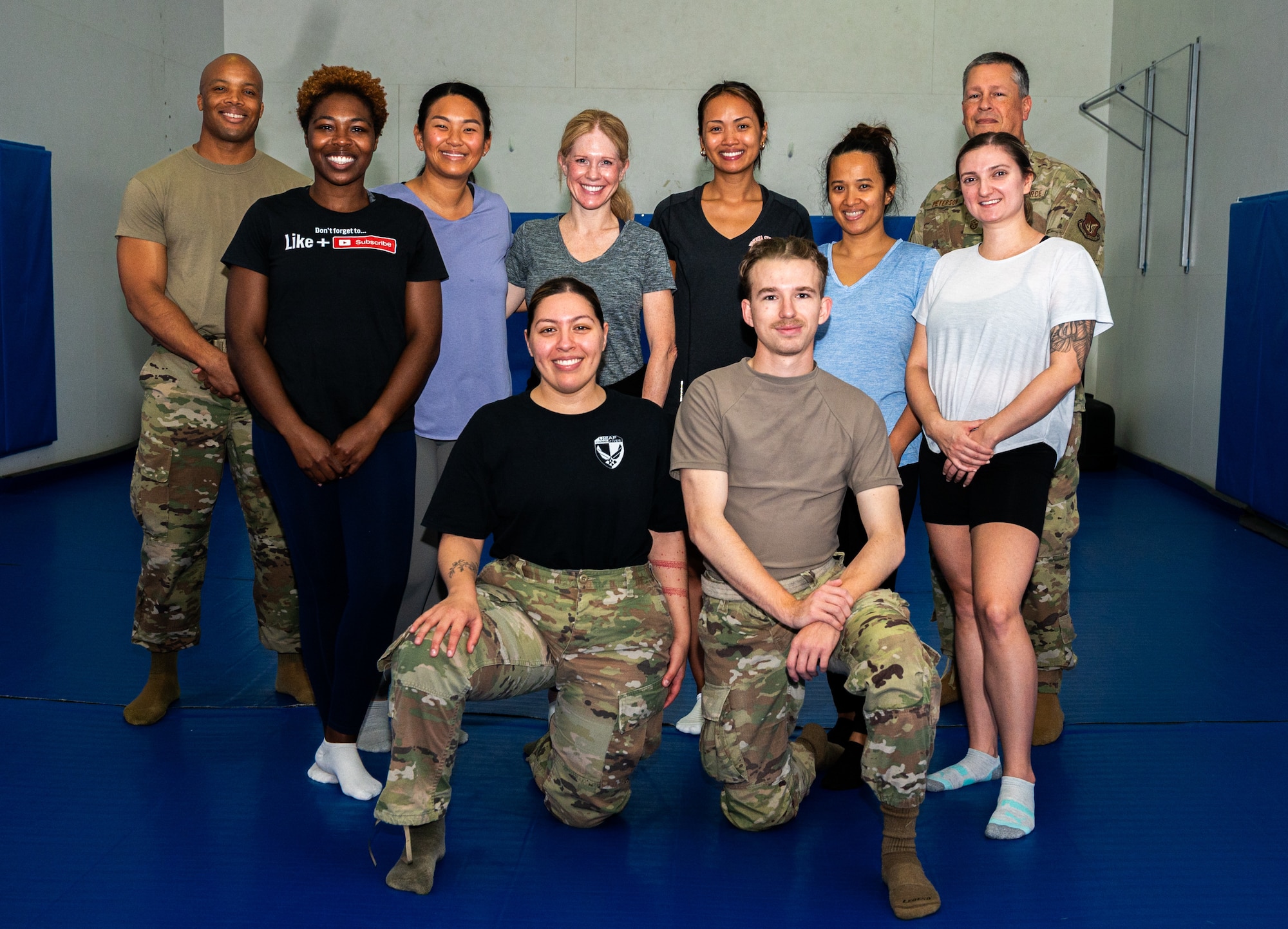 Airmen and participants pose for a photo on a blue mat during a self-defense basics course.