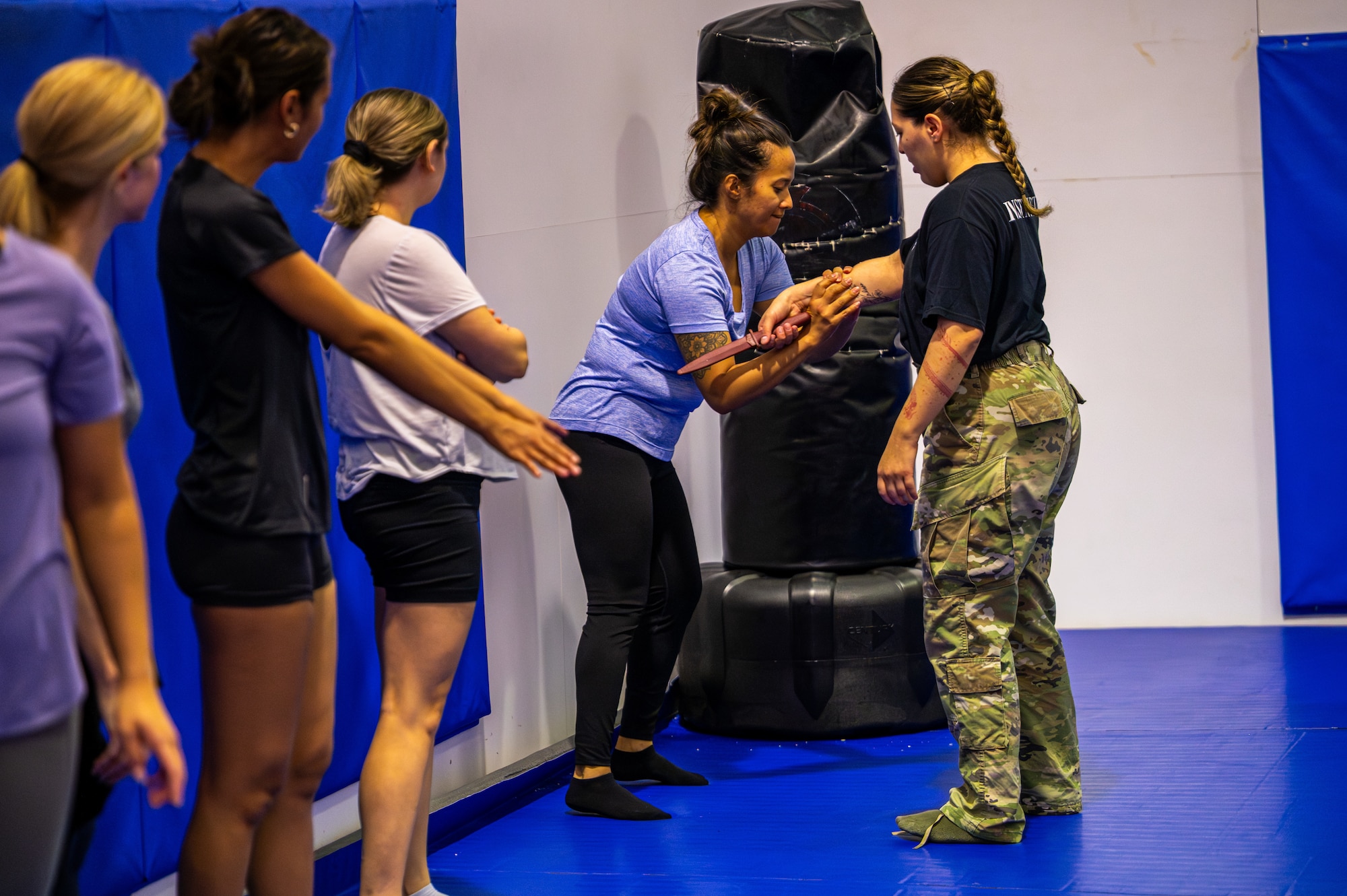 A person standing on a blue mat practices self defense measures against a simulated knife attack.