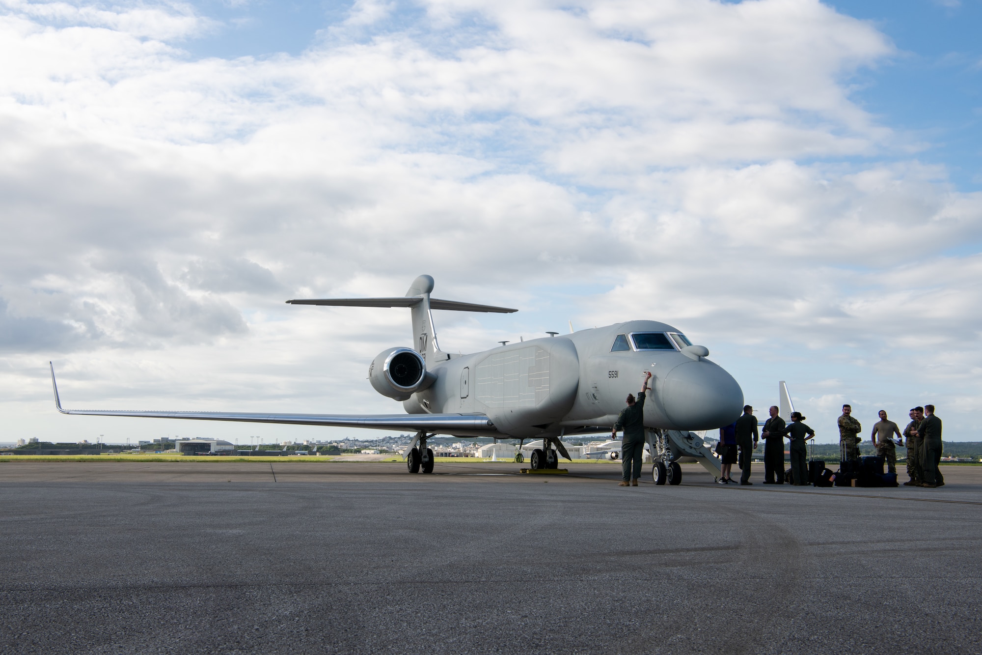 The right side of a white aircraft as it is parked on the flight line with aircrew unloading gear