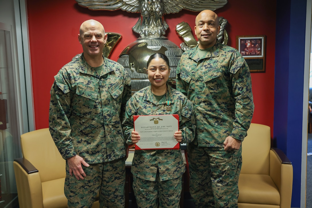 U.S. Marine Corps Maj. Gen. Walker M. Field, commanding general of Marine Corps Recruiting Command, left, and Sgt. Maj. Jesse J. Dorsey, MCRC sergeant major, right, award Cpl. Angela Garciasantos, unit diary clerk, with a Navy and Marine Corps Achievement Medal on Marine Corps Base Quantico, Va., Nov. 13, 2025. Garciasantos’ dedication to the recruiting mission resulted in her recognition as the MCRC Support Billet of the Year for Fiscal Year 2025. (U.S. Marine Corps photo by Cpl. Brenna Ritchie)