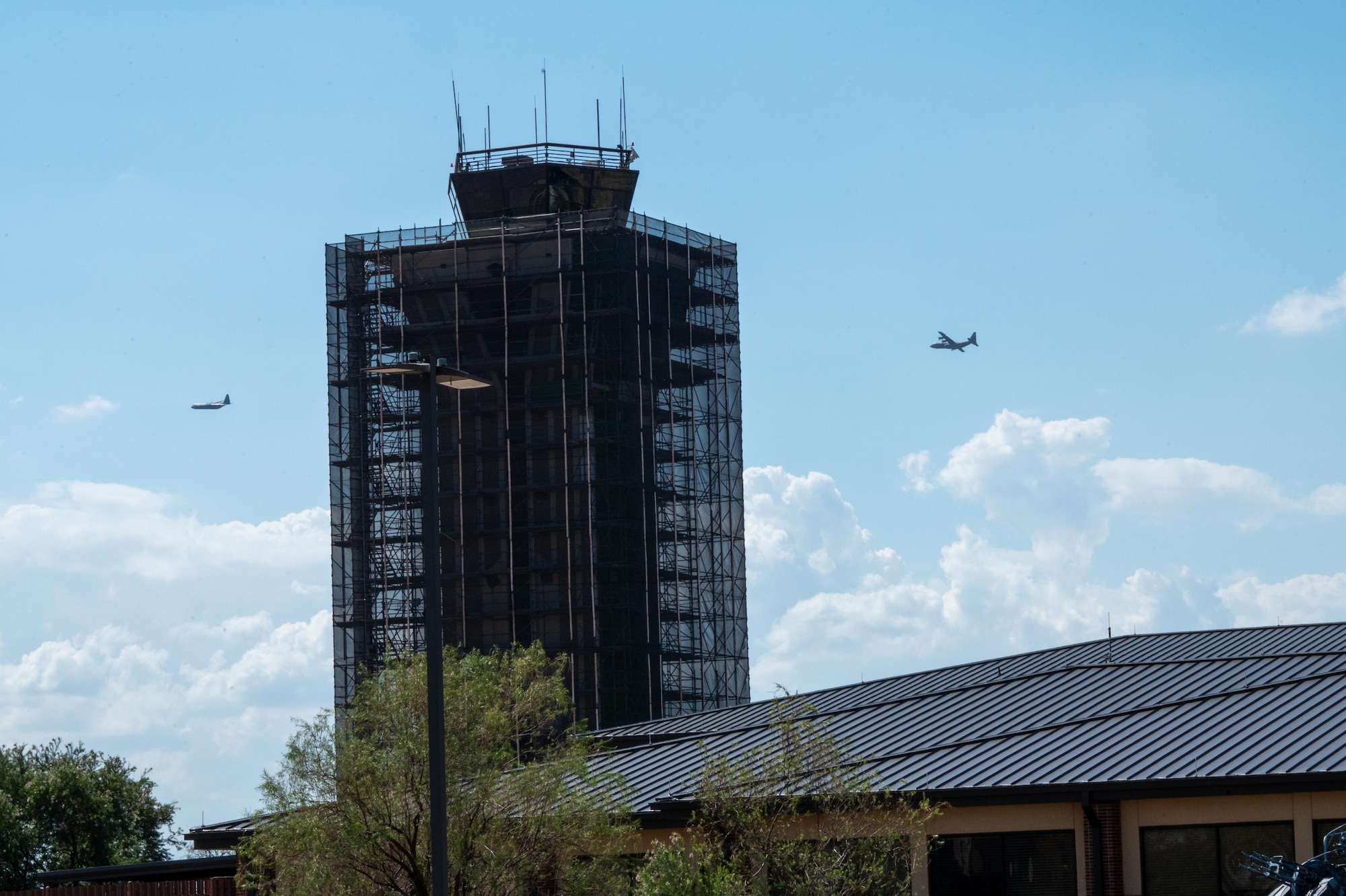 Two C-130 aircraft fly over a building