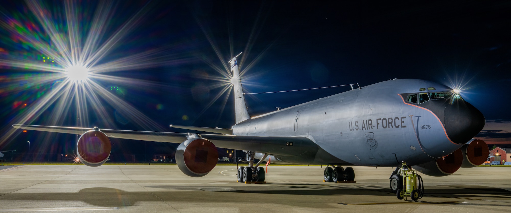 A KC-135 Stratotanker sites on a ramp in the dark while a flood light twinkles.