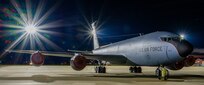 A KC-135 Stratotanker sites on a ramp in the dark while a flood light twinkles.