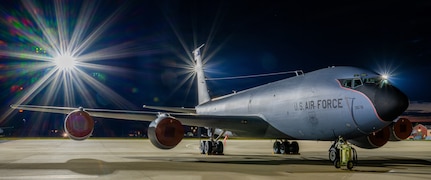 A KC-135 Stratotanker sites on a ramp in the dark while a flood light twinkles.