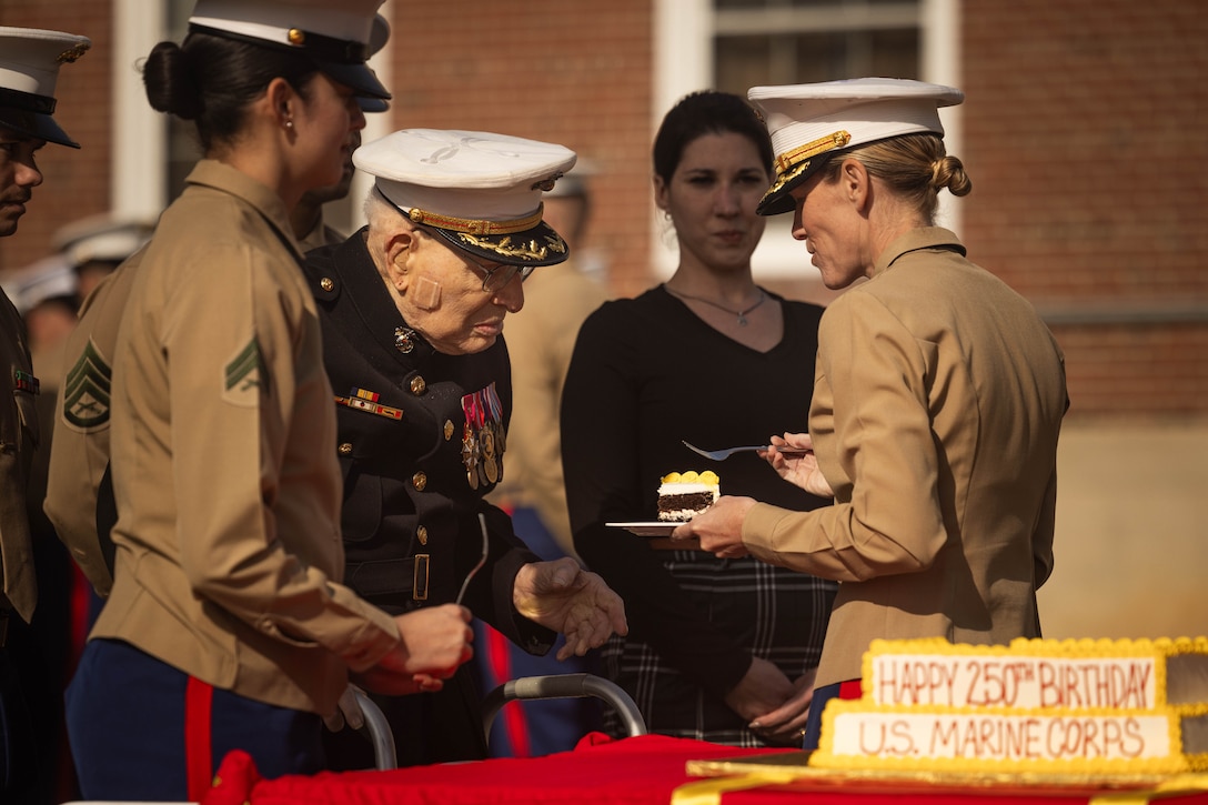 Retired U.S. Marine Corps Col. Frank Harris III, the oldest Marine in attendance, left, receives the first piece of cake from Col. Jenny Colegate, base commander of Marine Corps Base Quantico, during the Marine Corps cake cutting ceremony in honor of the 250th Marine Corps birthday at Lejeune Field on MCB Quantico, Virginia, Nov. 7, 2025. The ceremony honors the oldest and youngest Marine in attendance, representing the passing of tradition between generations of Marines. The annual celebration is a long-standing tradition which celebrates the establishment of the United States Marine Corps on Nov. 10, 1775, and honors the service and sacrifice of all Marines, past and present. (U.S. Marine Corps photo by Lance Cpl. Harleigh Faulk)