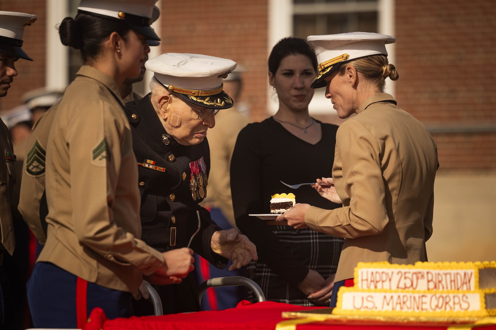 Retired U.S. Marine Corps Col. Frank Harris III, the oldest Marine in attendance, left, receives the first piece of cake from Col. Jenny Colegate, base commander of Marine Corps Base Quantico, during the Marine Corps cake cutting ceremony in honor of the 250th Marine Corps birthday at Lejeune Field on MCB Quantico, Virginia, Nov. 7, 2025. The ceremony honors the oldest and youngest Marine in attendance, representing the passing of tradition between generations of Marines. The annual celebration is a long-standing tradition which celebrates the establishment of the United States Marine Corps on Nov. 10, 1775, and honors the service and sacrifice of all Marines, past and present. (U.S. Marine Corps photo by Lance Cpl. Harleigh Faulk)