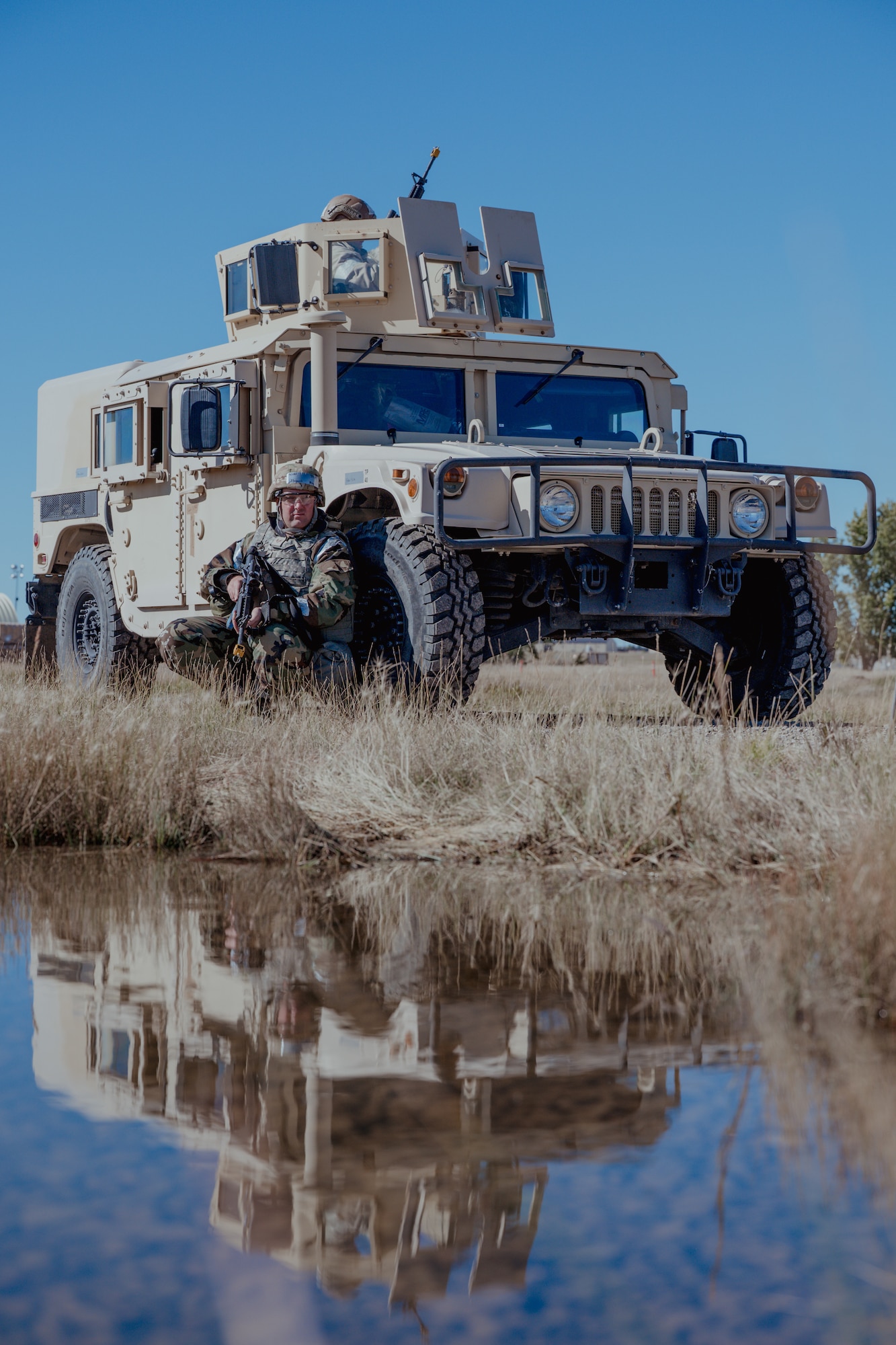 An Airman squatting and using an armored vehicle for cover.