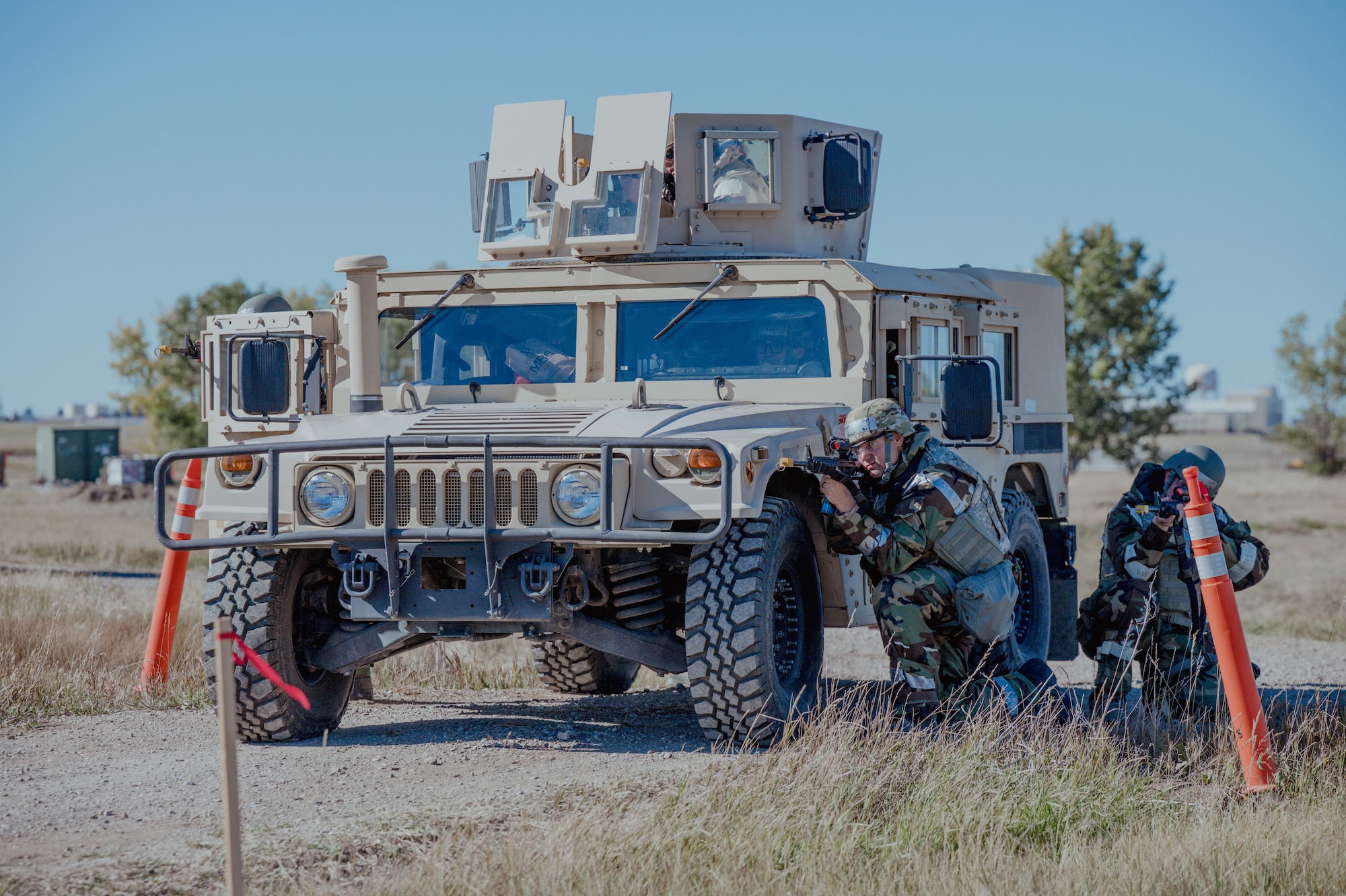 Airmen pointing weapons covered by an armored vehicle.
