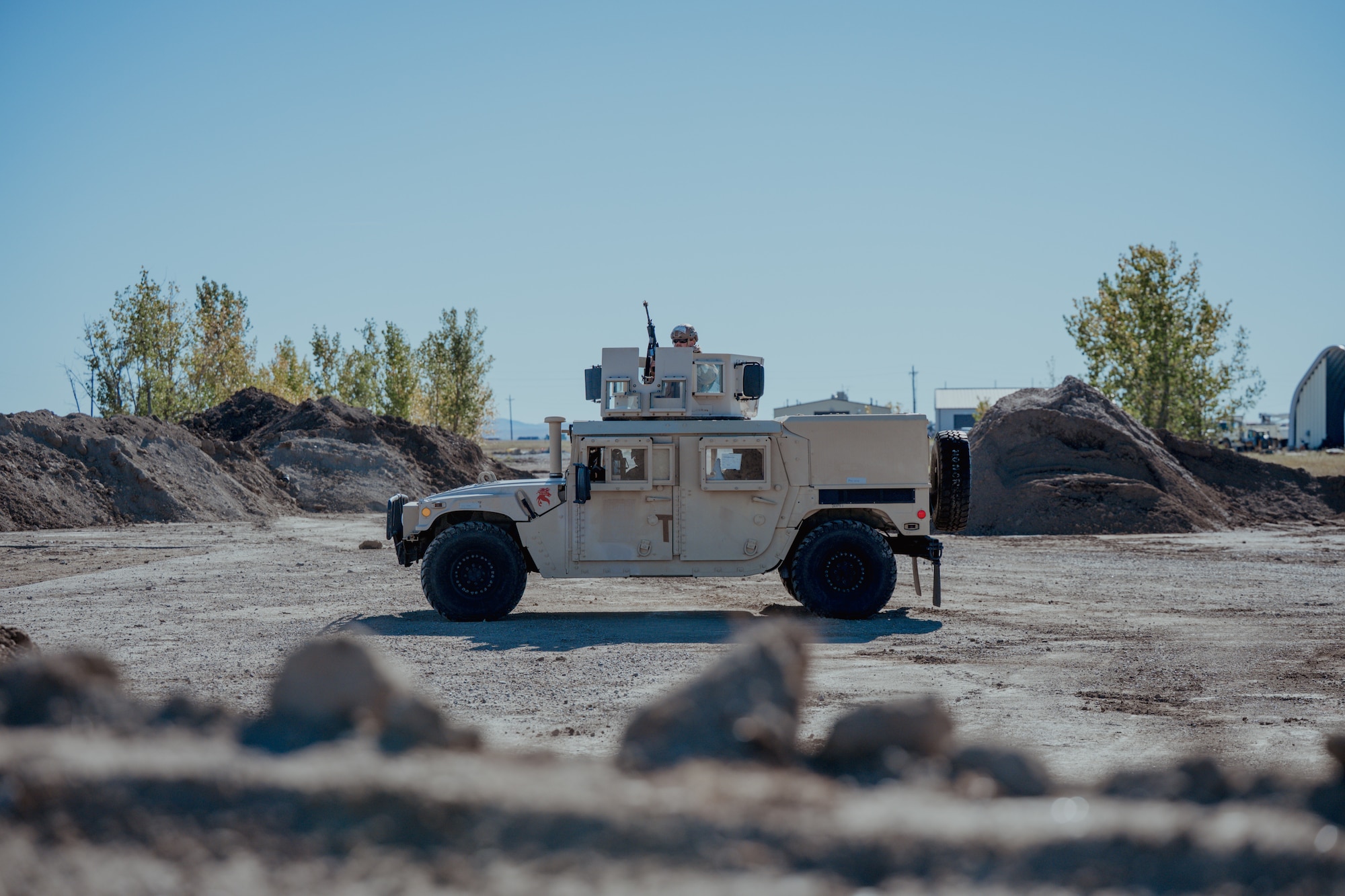 An armored vehicle is parked in between piles of dirt with an Airman on top.