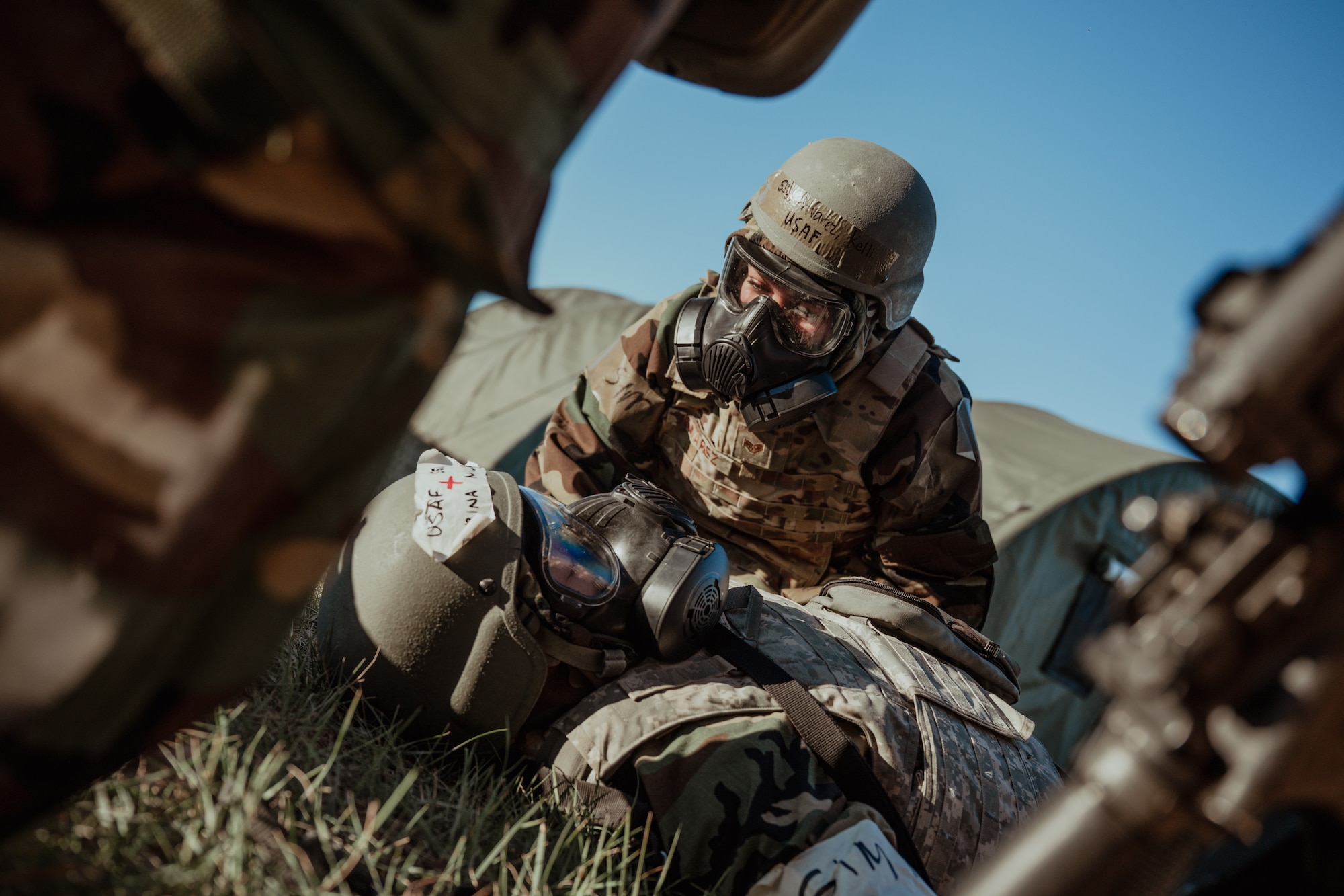 Airman wearing gas mask looking down at another Airman laying on the floor with a gas mask