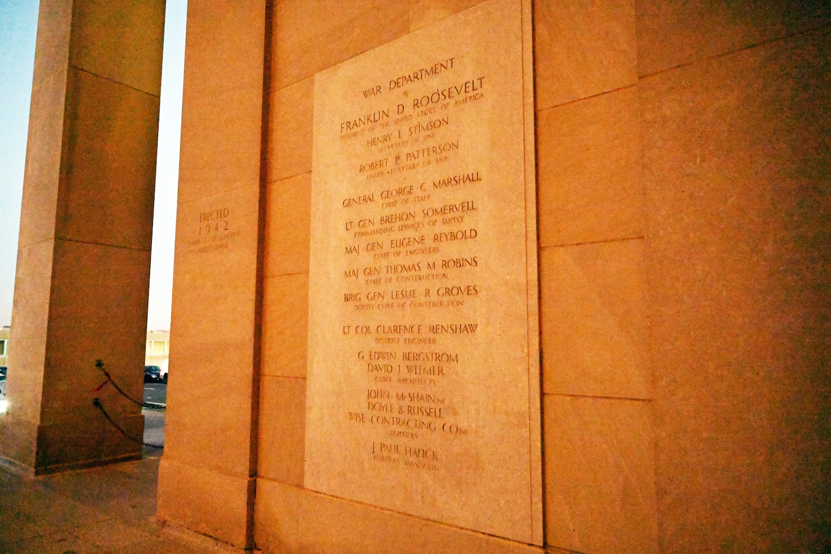 Names of individuals and jobs or positions are engraved into a stone plaque on a wall.