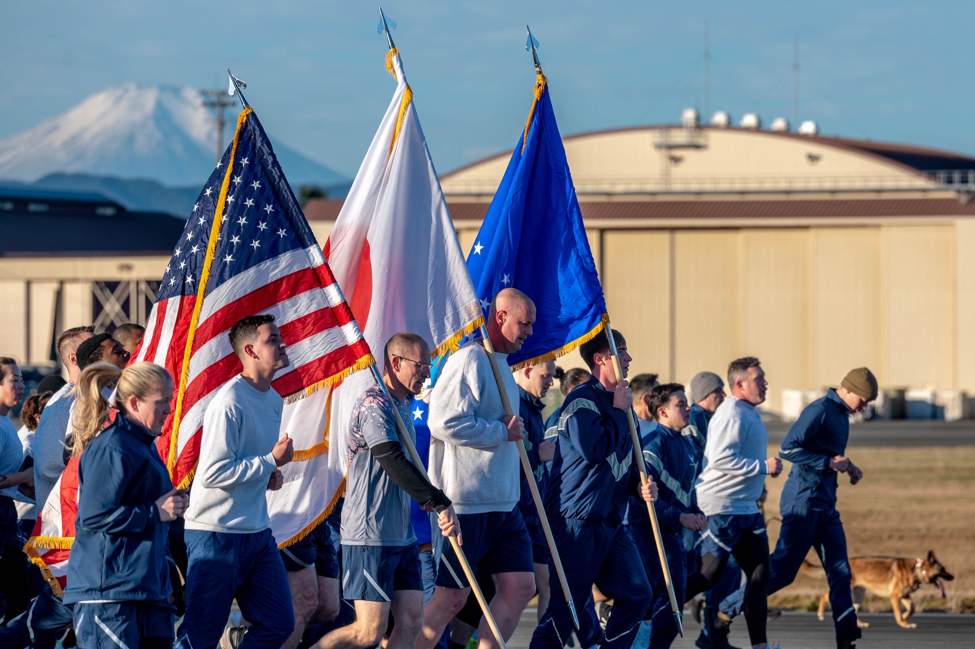 Military members in pt uniform run down the flightline.