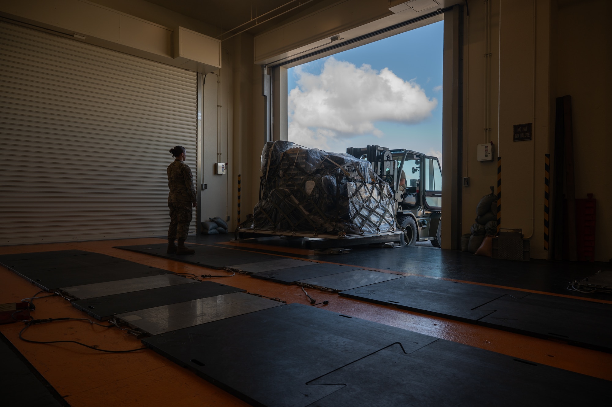 A service member stands by as cargo is offloaded by a forklift.
