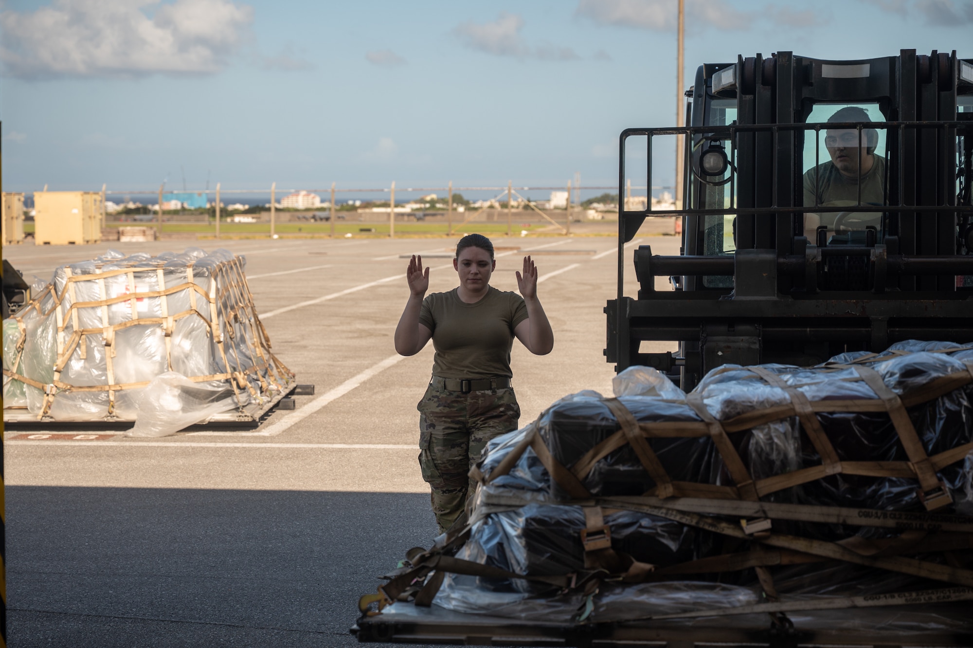 A service member guides a forklift operator while unloading cargo.