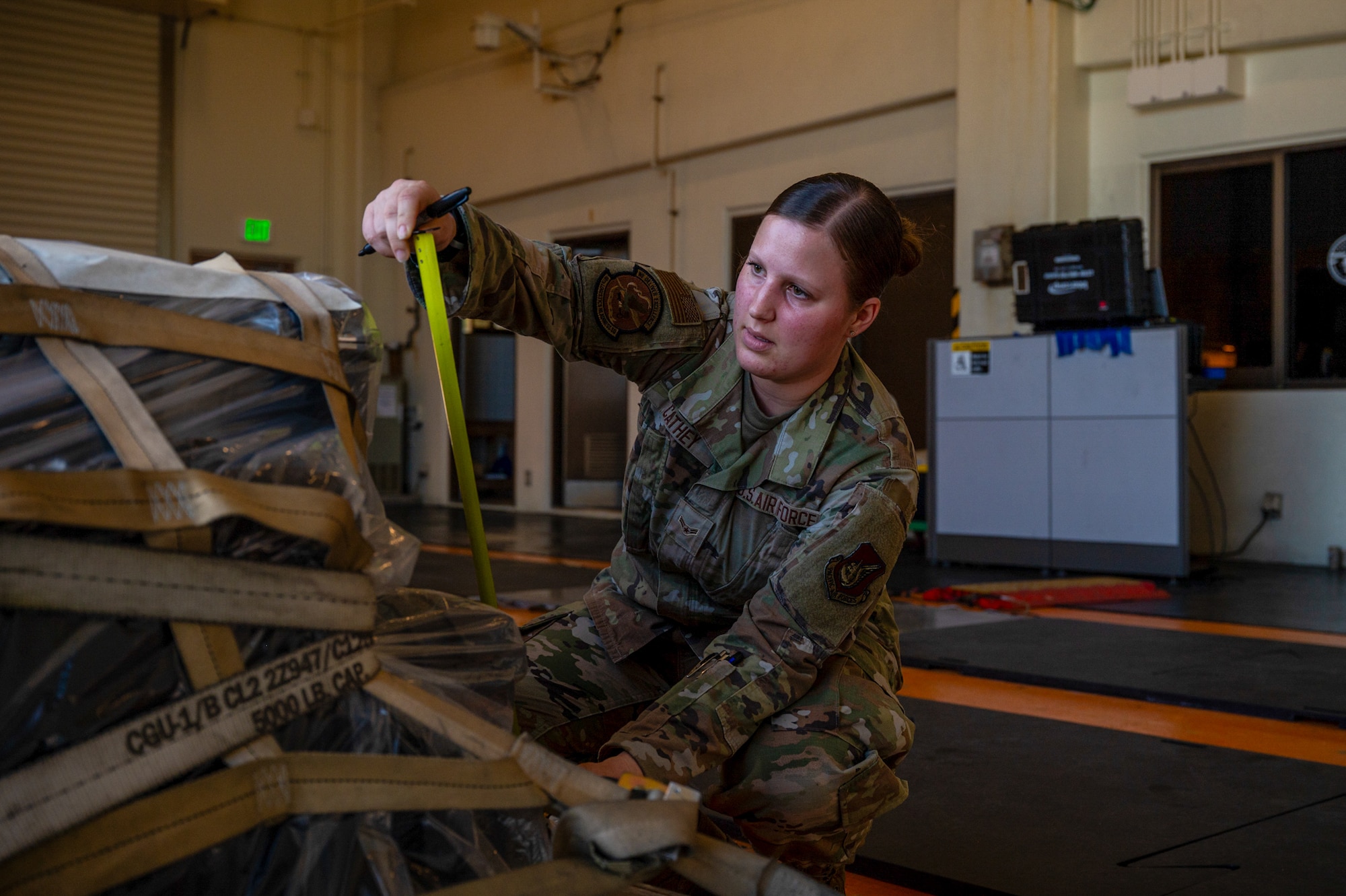 A service member measures a cargo pallet with a tape measure.