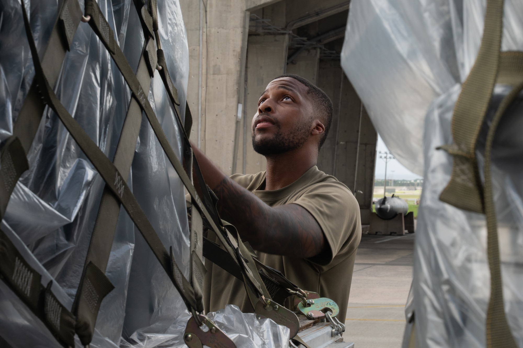 A military member secures cargo on a flatbed truck.