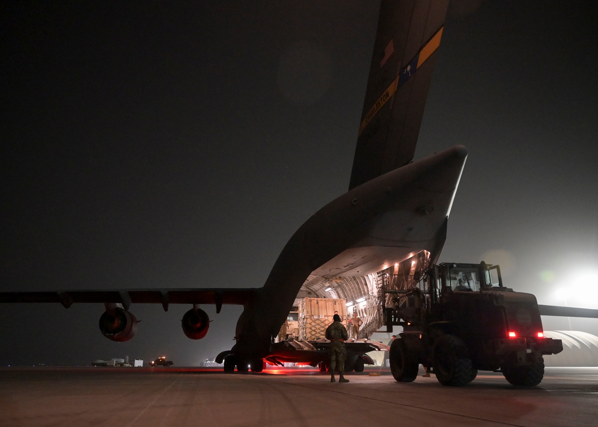 A large forklift approaches a large military aircraft.