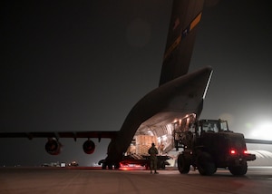 A large forklift approaches a large military aircraft.