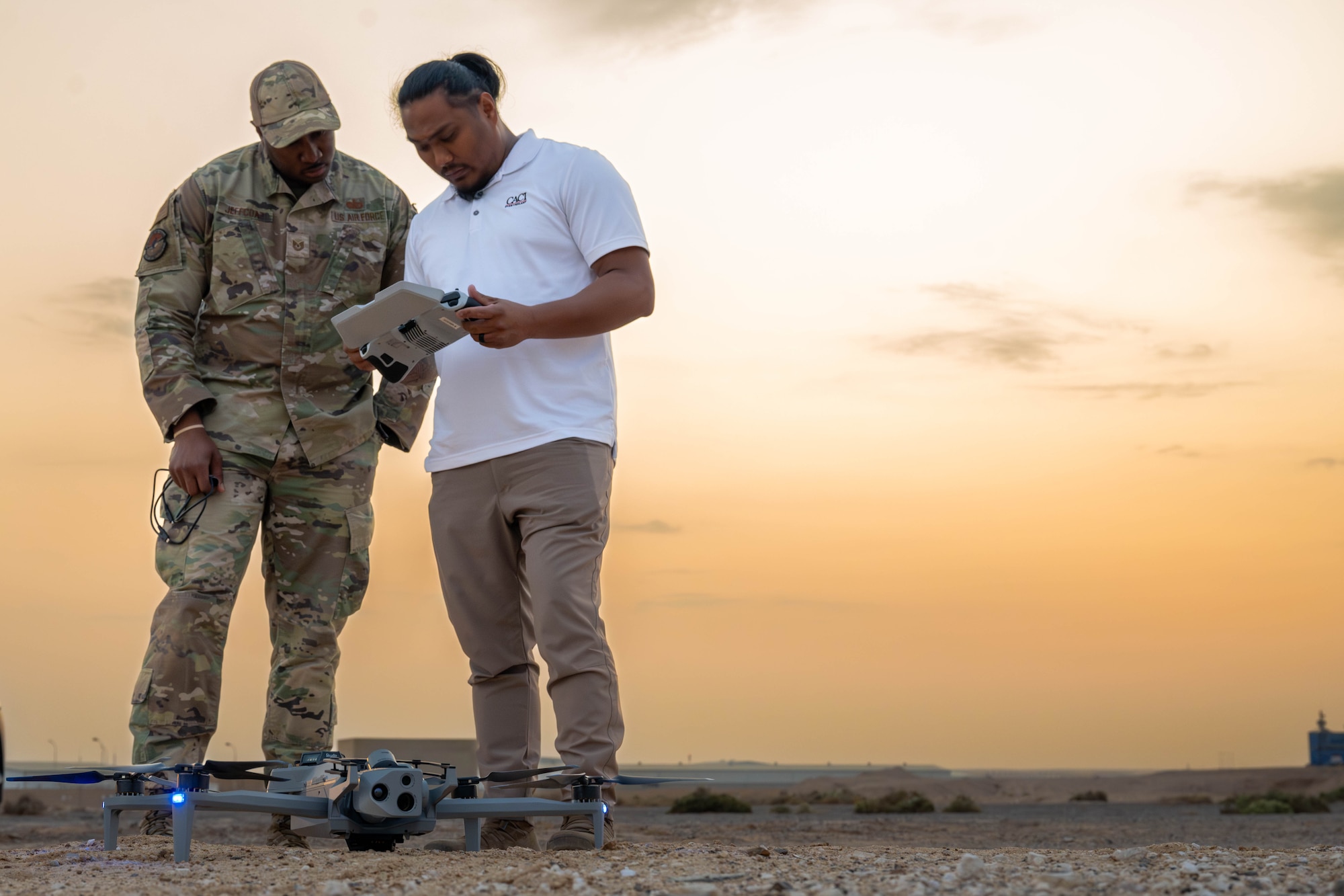 U.S. Air Force Tech. Sgt. Joshua Jeffcoat, 332nd Expeditionary Security Forces Squadron small unmanned aircraft systems program manager, watches  Manuel Ajoste, Consolidated Analysis Center International sUAS lead and evaluator control the quadcopter in the U.S. Central Command area of responsibility, Nov. 4, 2025. The quadcopter is equipped with multiple camera capabilities, including a 360-degree field of view, thermal imaging and advanced high-resolution zoom, giving defenders a detailed look at their surroundings to view threats. (U.S. Air Force photo by Senior Airman Kari Degraffenreed)