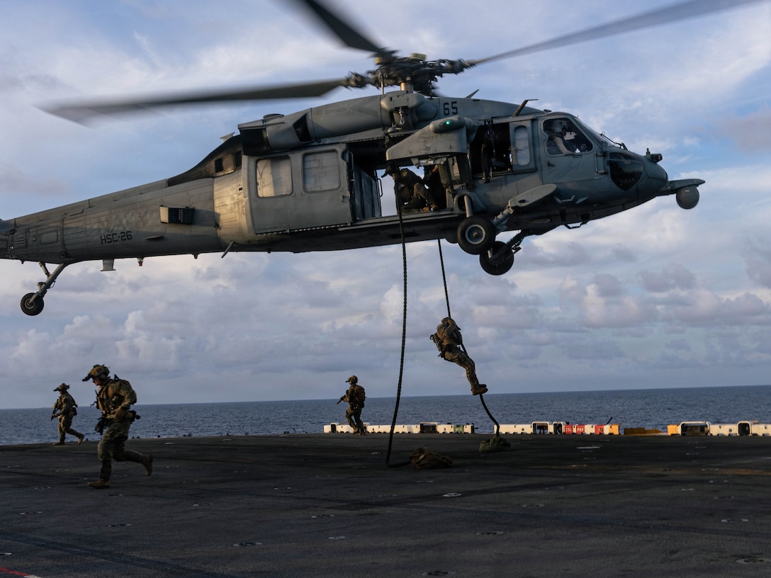 CARIBBEAN SEA – U.S. Marines with Maritime Special Purpose Force, 22nd Marine Expeditionary Unit (Special Operations Capable), fast-rope out of a U.S. Navy MH-60S Sea Hawk helicopter with Helicopter Sea Combat Squadron (HSC) 26, Iwo Jima Amphibious Ready Group, during fast rope insertion drills aboard Wasp-class amphibious assault ship USS Iwo Jima (LHD 7) while underway in the Caribbean Sea, Oct. 23, 2025. U.S. military forces are deployed to the Caribbean in support of the U.S. Southern Command mission, Department of War-directed operations, and the president’s priorities to disrupt illicit drug trafficking and protect the homeland. (U.S. Marine Corps photo by Sgt. Tanner Bernat)