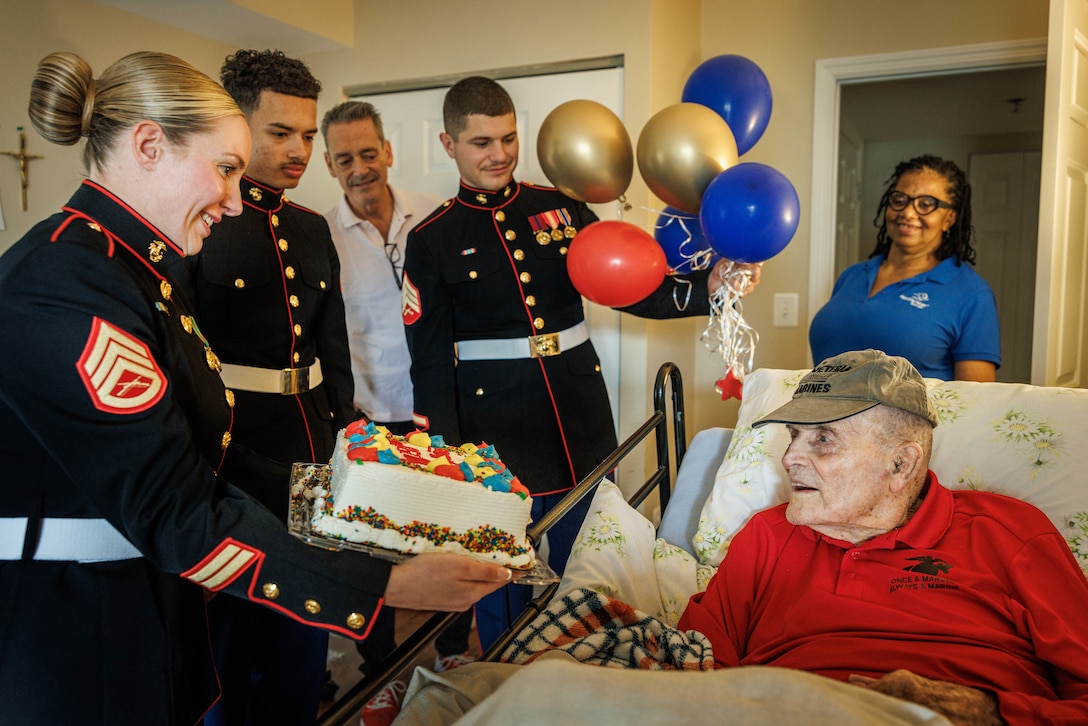Marine Corps Base Quantico’s Ceremonial Platoon presents U.S. Marine Corps Pfc. John Grimes, a World War II veteran, with a cake to celebrate the upcoming 250th birthday of the Marine Corps at The Jefferson, Arlington, Virginia, Oct. 10, 2025. Grimes enlisted in the Marine Corps in 1943 and became a radio operator and fought in WWII during the battle of Tinian in 1944. During the battle he was injured by a mortar blast and later awarded the Purple Heart. (U.S. Marine Corps photo by Lance Cpl. Harleigh Faulk)