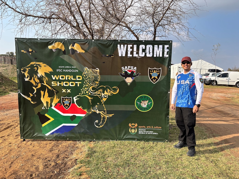 United States Air Force Tech Sgt. Dan Antonio Deladingco, 9th Mission Support Group (MSG) executive assistant, poses next to a sign advertising the 2025 International Practical Shooting Confederation (IPSC) Handgun World Shoot in Stilfontein, South Africa, Aug. 22, 2025.