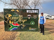 United States Air Force Tech Sgt. Dan Antonio Deladingco, 9th Mission Support Group (MSG) executive assistant, poses next to a sign advertising the 2025 International Practical Shooting Confederation (IPSC) Handgun World Shoot in Stilfontein, South Africa, Aug. 22, 2025.