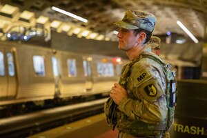 A man dressed in a camouflage military uniform stands on a subway platform.