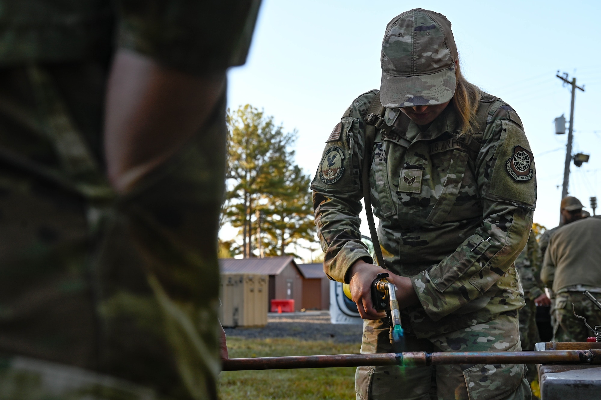 A woman in uniform applies a blowtorch to a metal pipe.