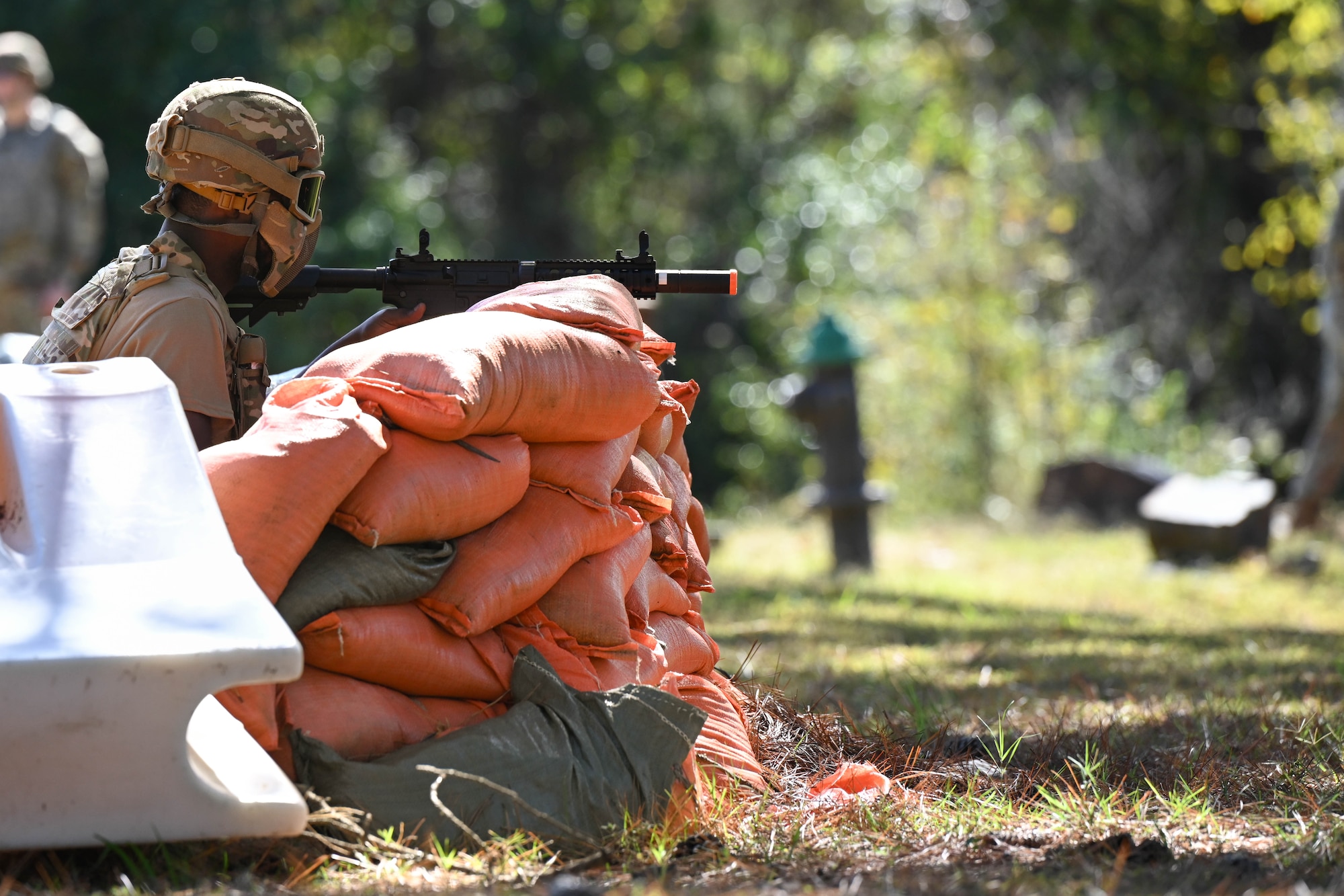 A man in uniform sits behind a sandbag fortification.