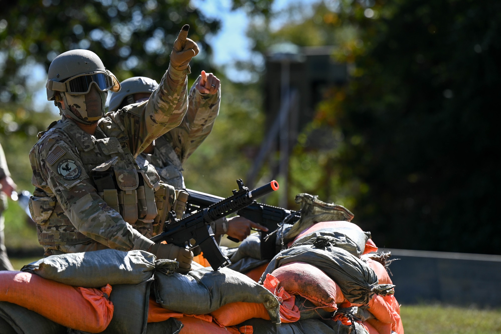 A group of men in uniform sit behind a sandbag fortification