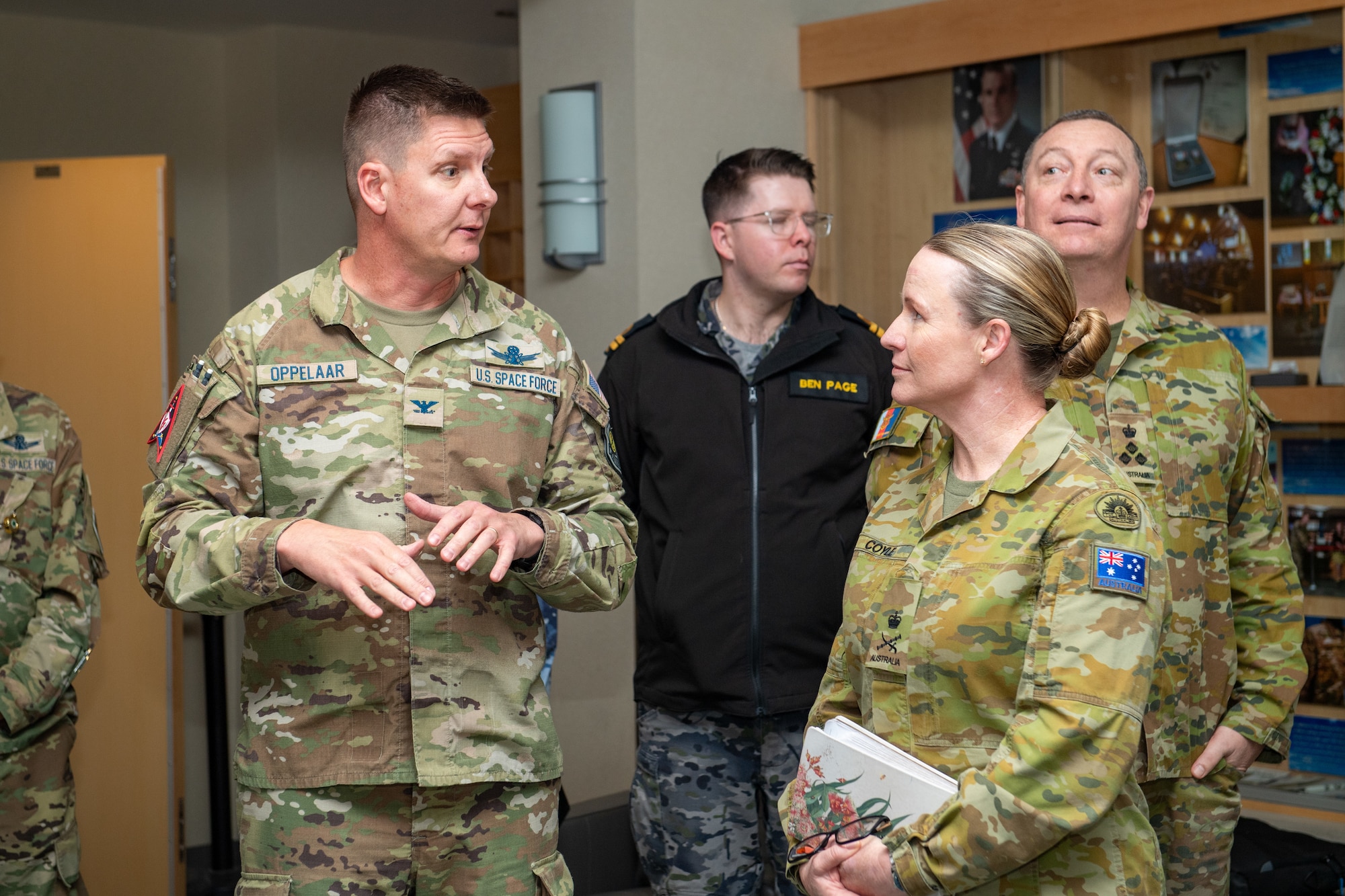 A uniformed man talks to a uniformed woman motioning with his hands. The woman listens intently while other uniformed members look around the space behind them