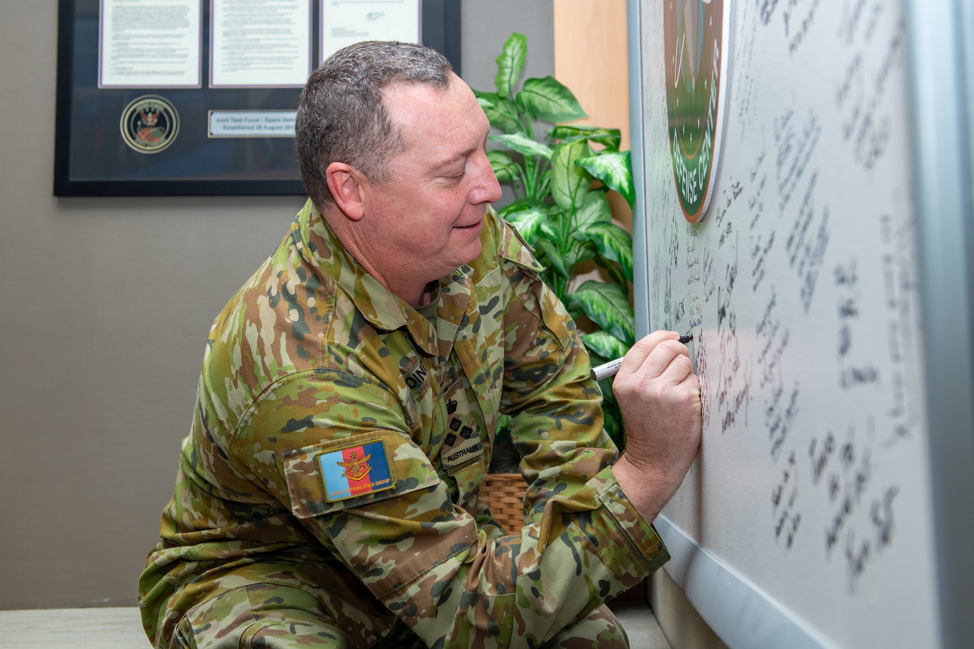 A uniformed man smiles as he writes on a whiteboard