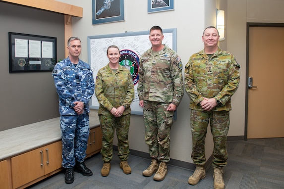 Four uniformed service members stand together, smiling, in front of a whiteboard with signatures on it.