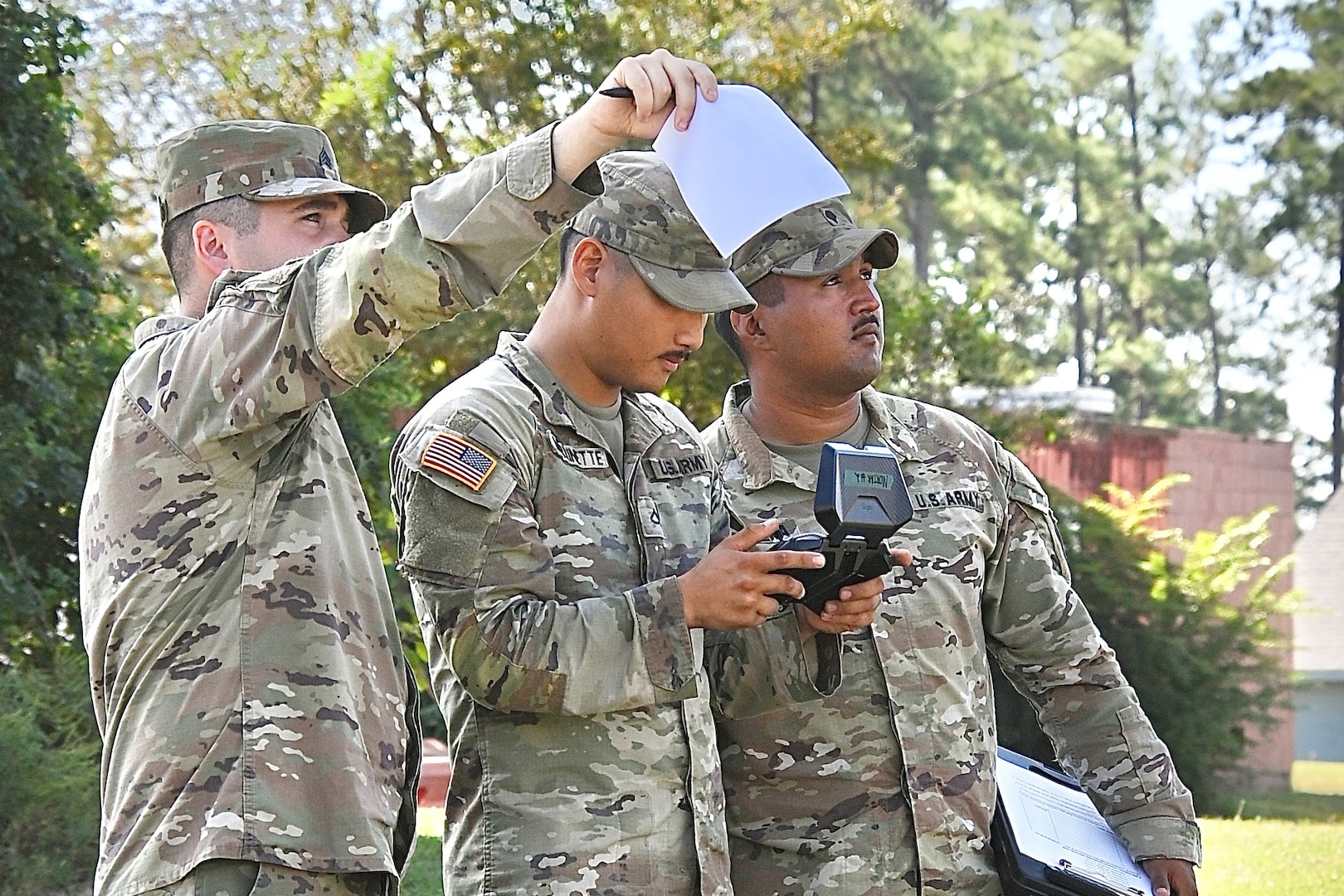 Three Soldiers stand together. One points to the sky, one observes, and one operates a drone with a hand-held controller.