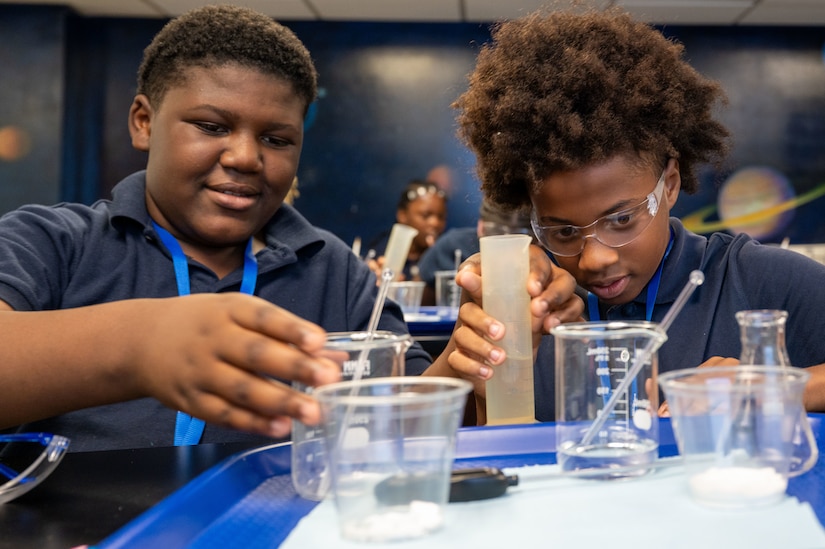 Two children wearing polo shirts hold laboratory equipment while conducting an experiment in a science lab.