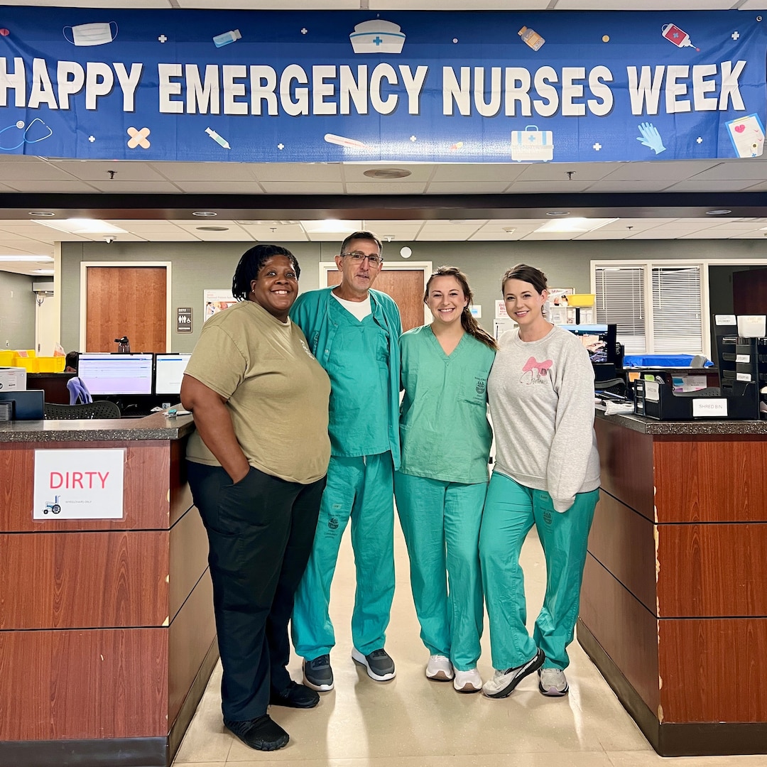 Four Emergency Nurses in scrubs stand under a banner that reads "Happy Emergency Nurses Week."