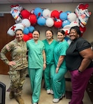 Five Emergency Nurses stand in front of a large balloon wreath. One is in uniform, the others in scrubs.