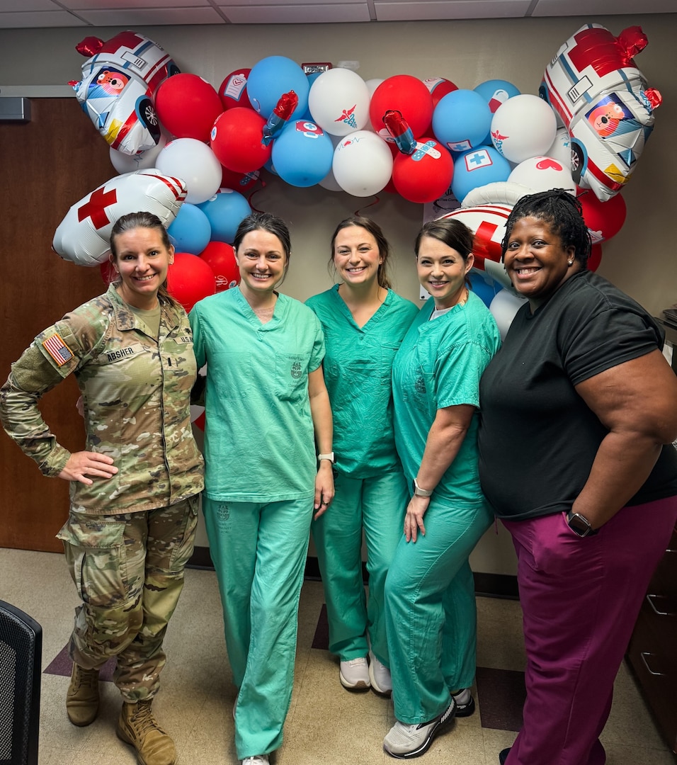 Five Emergency Nurses stand in front of a large balloon wreath. One is in uniform, the others in scrubs.