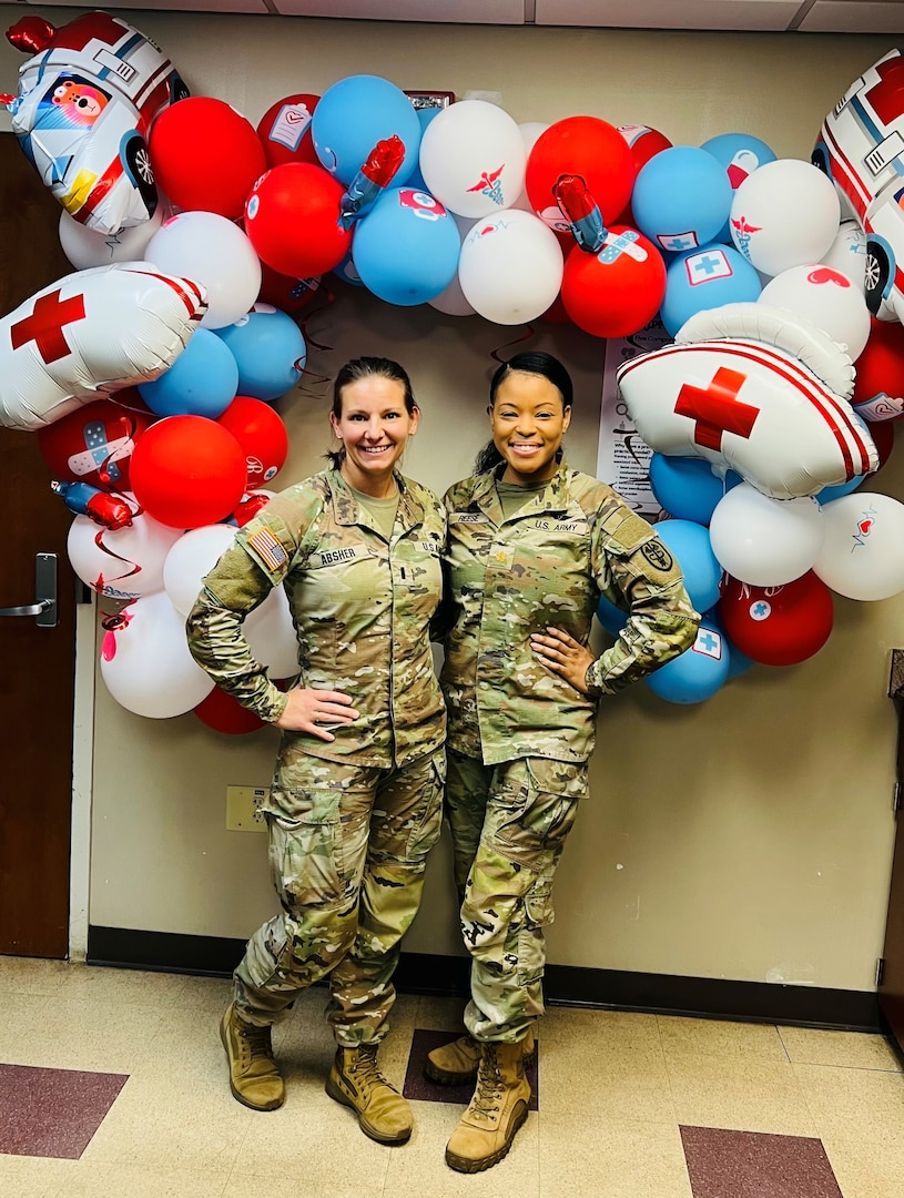 Two Soldier nurses stand in front of a large balloon wreath.