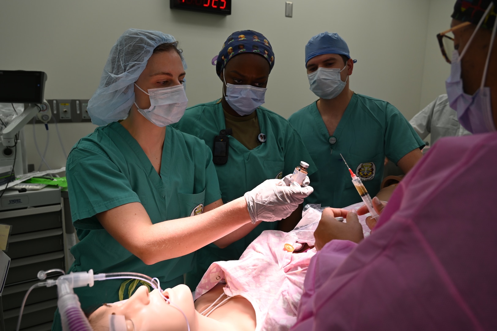 Dr. Jessica Ulinski, a board-certified nurse anesthetist and leader of the training simulation, reviews a vial of medication while a nurse prepares a syringe, with team members watching closely during the training session.