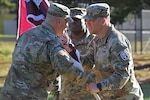 Two Soldiers pass the unit guidon (flag) on a parade field.