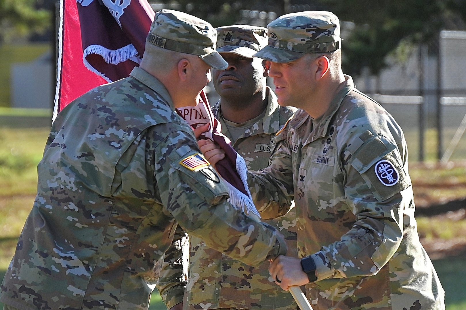 Two Soldiers pass the unit guidon (flag) on a parade field.