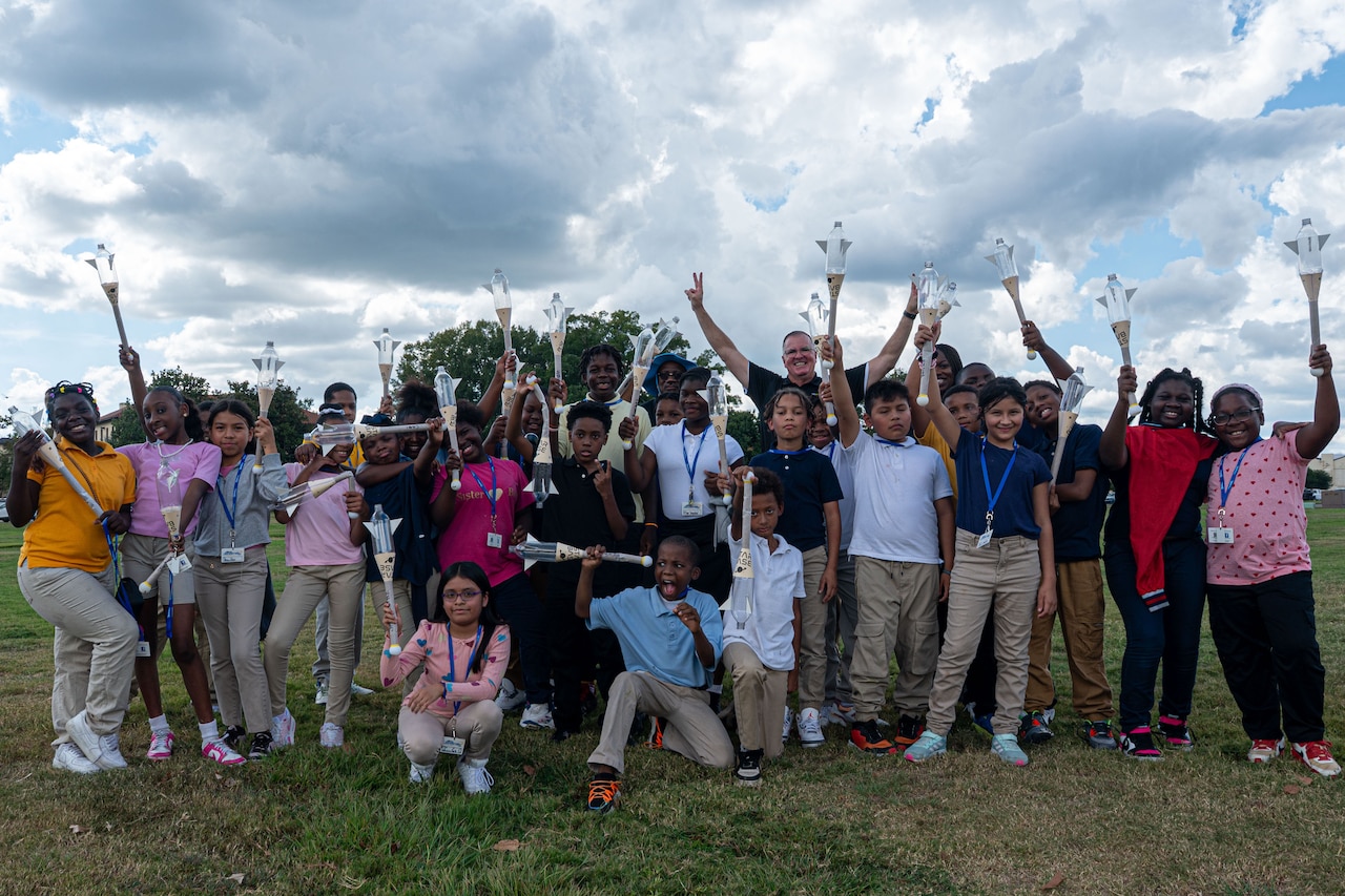 A group of children and their teachers pose for a photo. The children are holding model rocket ships.